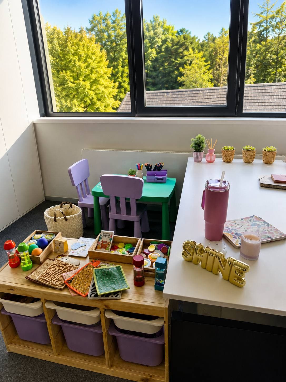 A children's corner by the window: a green table, two small chairs and a shelf with storage boxes