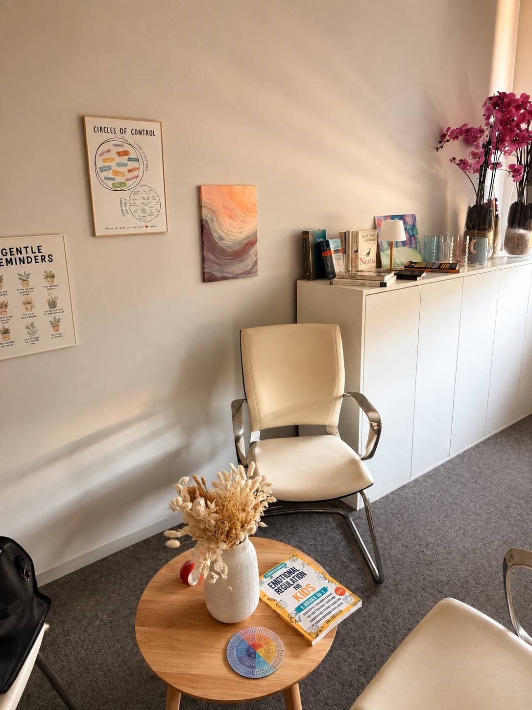A light therapy room: an armchair, a round table with dried flowers and posters on the wall